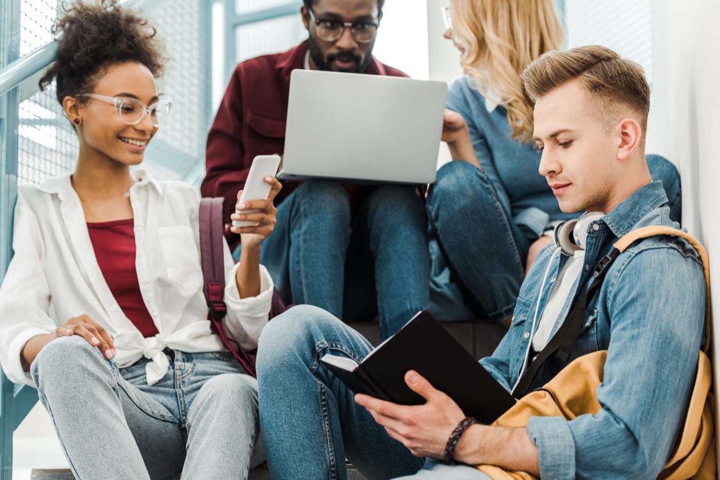 Four smiling multiethnic students using laptop and tablet together